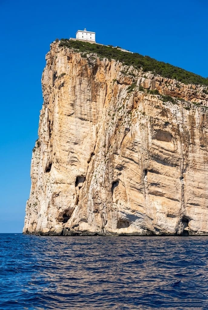 Una prospettiva verticale imponente della scogliera di Capo Caccia e del suo faro ad Alghero, vista dal mare durante un'escursione in barca.