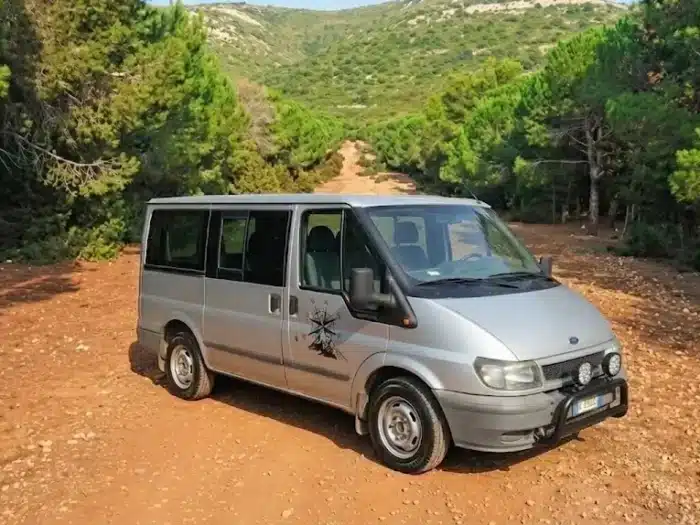 Tavola imbandita in un agriturismo tipico ad Alghero, con piatti di pasta fresca (malloreddus o culurgiones), taglieri di salumi e formaggi sardi, pane carasau e vino rosso.