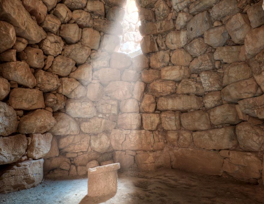 Interno di un nuraghe sardo con un raggio di luce solare che illumina un altare in pietra, tappa archeologica di un tour in van ad Alghero.